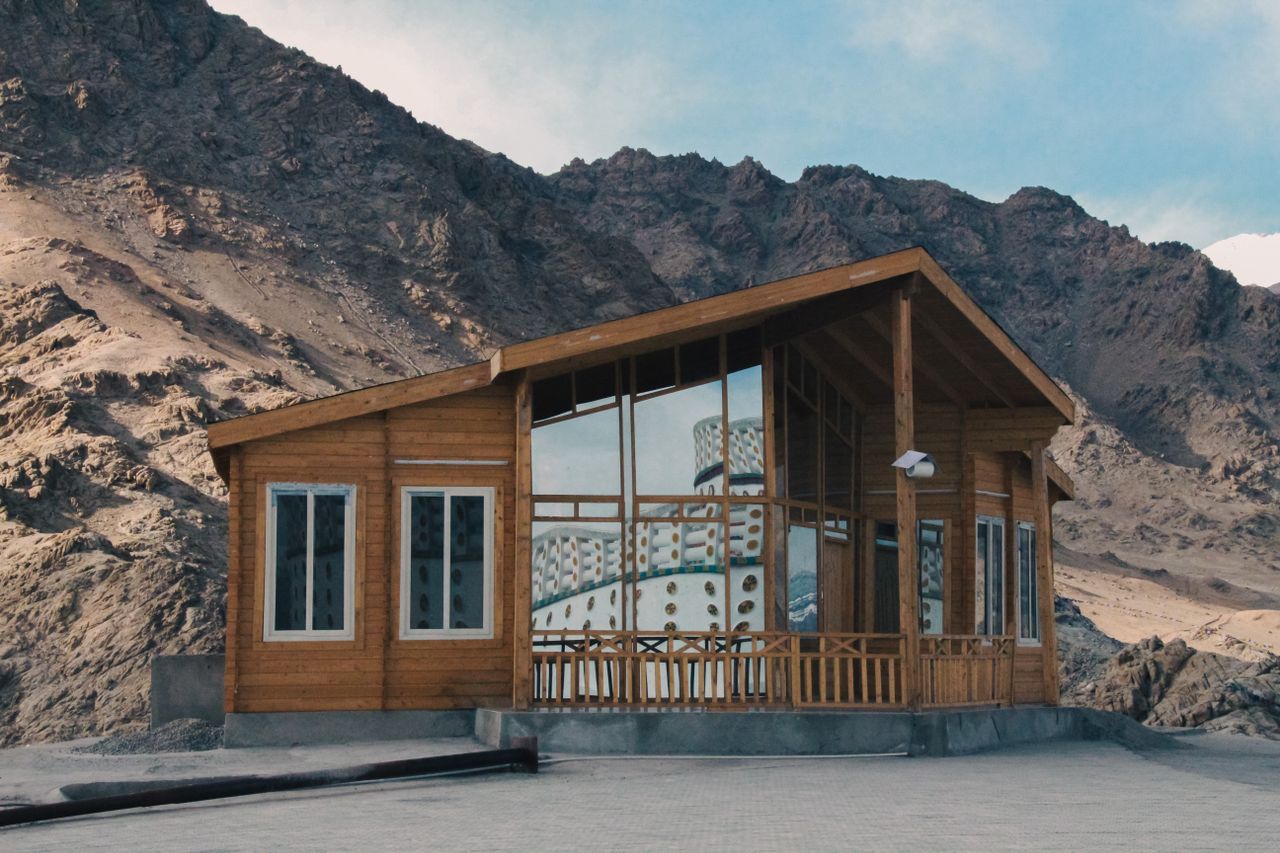 A wooden cabin standing alone in a mountainous landscape under a clear blue sky.